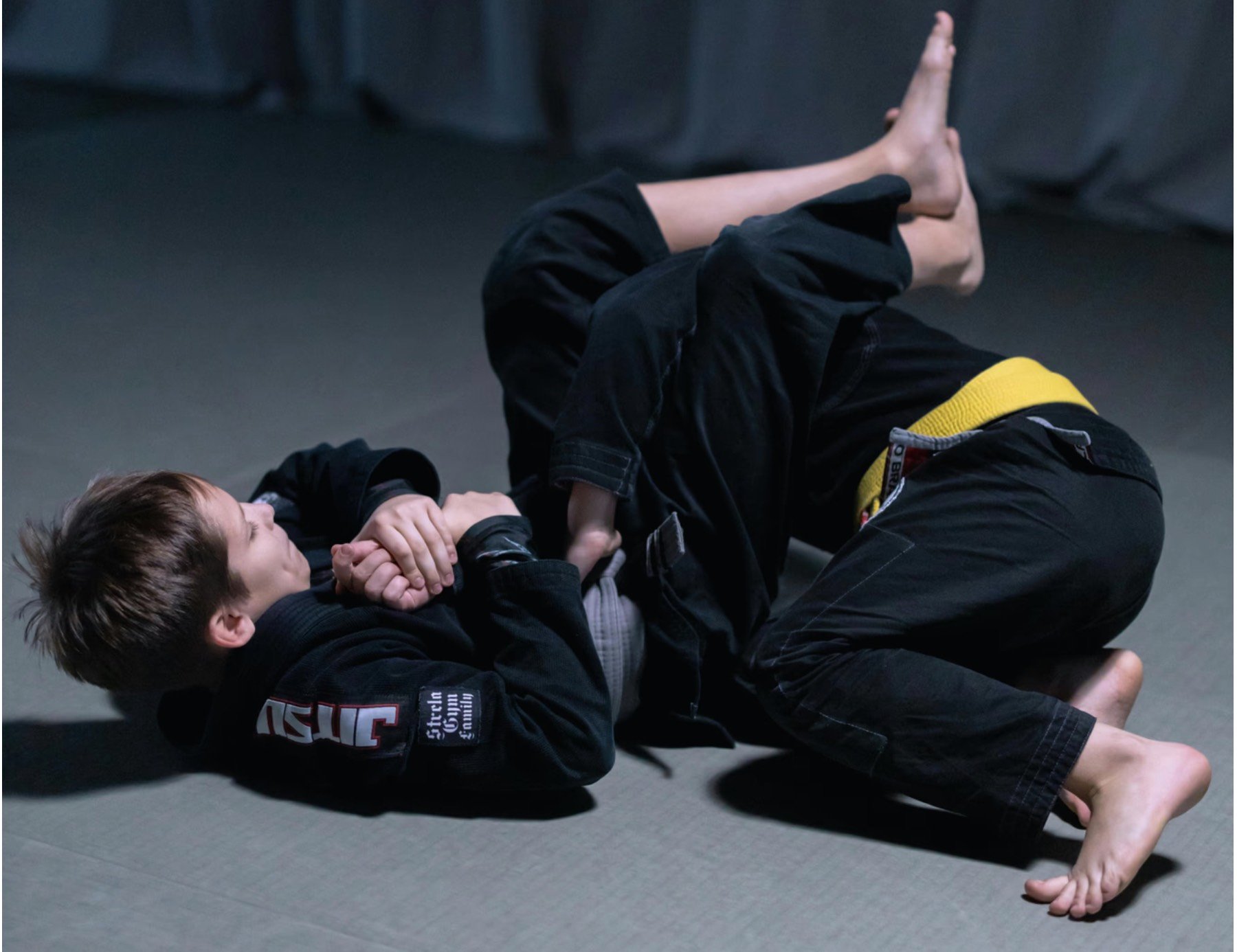 Niños con gi de BJJ practicando técnicas en el tatami de una academia de artes marciales