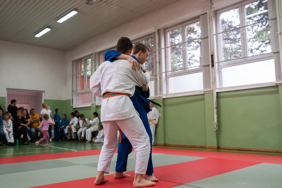 Dos judocas practicando agarres mientras otros alumnos observan
