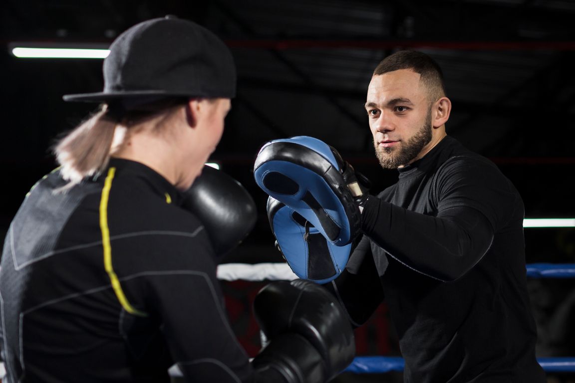 Mujer con guantes de boxeo practicando con las manoplas de su entrenador