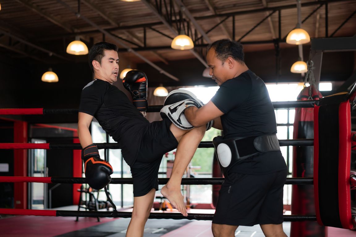 Practicante de Muay Thai entrenando un golpe de rodilla con un entrenador que sostiene paos