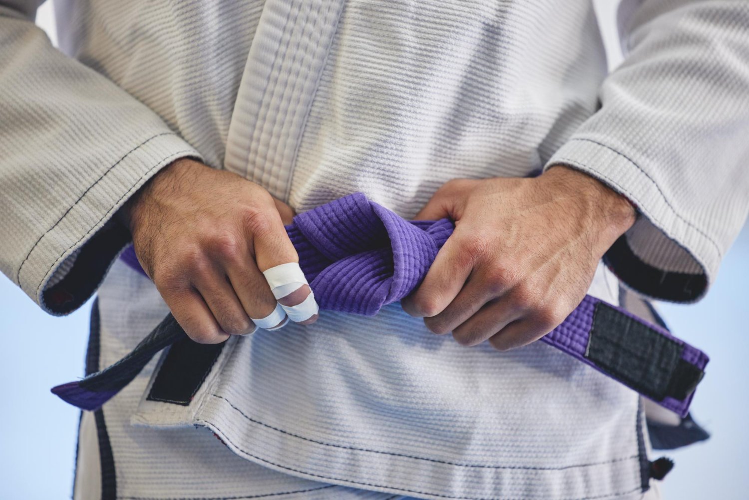 Practicante de BJJ anudando un cinturón morado antes del entrenamiento