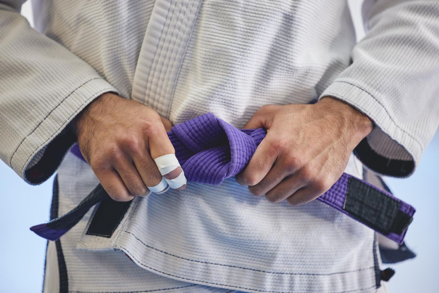 Practicante de BJJ anudando un cinturón morado antes del entrenamiento