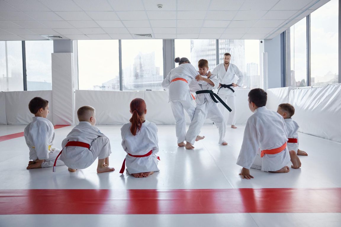 Niños practicando artes marciales mientras su instructor y sus compañeros observan